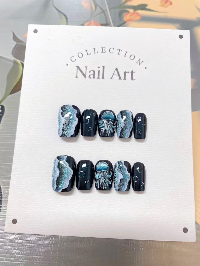 Peut inclure: Ensemble de faux ongles avec une base bleu fonc&eacute;. Certains ongles pr&eacute;sentent un motif tourbillonnant bleu et blanc, tandis que d'autres pr&eacute;sentent une illustration de m&eacute;duse. Le texte "Collection Nail Art" est visible.