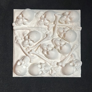 May include: A white ceramic wall sculpture featuring a pile of skulls and bones. The skulls are arranged in a random pattern and the bones are intertwined with the skulls.