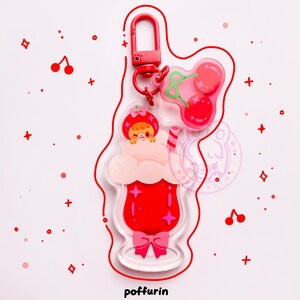 Op de afbeelding: Een heldere acryl sleutelhanger met een rood drankje met een roze strik, een stripfiguur met een aardbeienhoed en een kersendesign. De sleutelhanger heeft een rode sluiting en de tekst "poffurin" onderaan.