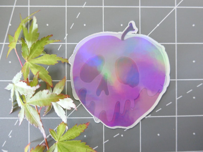 May include: A holographic sticker of a purple apple with a skull face. The apple is dripping with purple liquid.