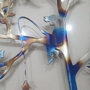 Puede incluir: Una escultura de pared de metal de un &aacute;rbol con una ni&ntilde;a sentada en una rama y pescando. El &aacute;rbol est&aacute; hecho de metal y tiene un acabado azul y dorado. La ni&ntilde;a tambi&eacute;n est&aacute; hecha de metal y tiene un acabado azul.