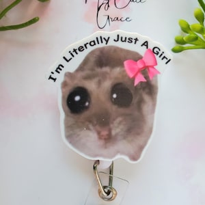 May include: A white plastic badge holder with a picture of a brown and white animal with large eyes and a pink bow. The text "I'm Literally Just A Girl" is printed around the picture.