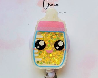 May include: A white and blue baby bottle shaped retractable badge holder with a pink lid and gold glitter inside. The bottle has a cute cartoon face with black eyes and a smile. The badge holder is attached to a silver chain.