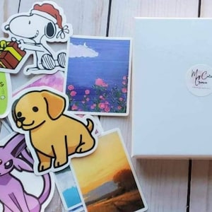 May include: A set of stickers featuring a variety of designs, including a cartoon dog, a cartoon cat, a cartoon character wearing a Santa hat, a sunset landscape, a floral landscape, and a cartoon character with a third eye. The stickers are on a white background with a white box in the background. The box has a sticker on it that says "My Cute Grace".