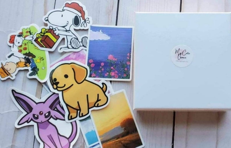 May include: A set of stickers featuring a variety of designs, including a cartoon dog, a cartoon cat, a cartoon character wearing a Santa hat, a sunset landscape, a floral landscape, and a cartoon character with a third eye. The stickers are on a white background with a white box in the background. The box has a sticker on it that says "My Cute Grace".