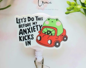 May include: A white badge reel with a cartoon frog driving a red car. The text reads "Let's Do This Before My Anxiety Kicks In." The badge reel has a clear plastic strap and a metal clip.