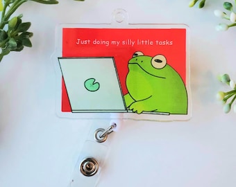 May include: A clear acrylic badge holder with a red background and a cartoon frog using a laptop. The text on the badge holder reads "Just doing my silly little tasks."