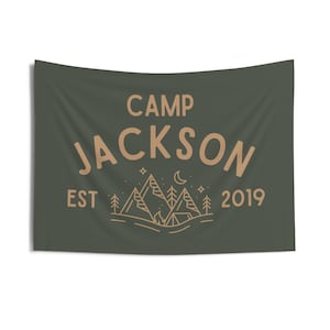 May include: A green camping flag with the text "Camp Jackson Est 2019" and a line drawing of mountains, a campfire, and a crescent moon.