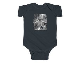 May include: A dark blue baby onesie with a silver graphic of Jean-Jacques Dessalines, a Haitian revolutionary leader, with the text "Jean-Jacques Dessalines" in a silver font.