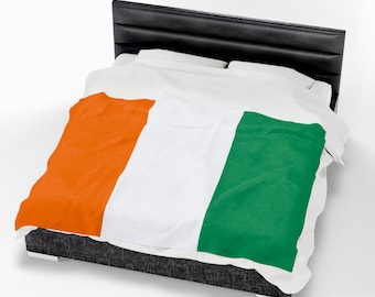 May include: A bed with a black headboard and a blanket featuring the flag of Ivory Coast. The blanket has vertical stripes of orange, white, and green. The bed frame is dark gray.