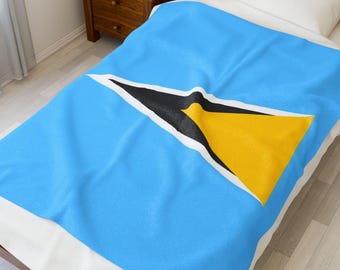 May include: A light blue blanket with the flag of Saint Lucia displayed prominently. The flag features a yellow triangle, a black triangle, and a white border. The blanket is on a bed with a white pillow.