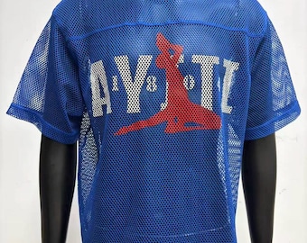 May include: A bright blue short-sleeved mesh jersey featuring the white text AYITI with a red silhouette of a person sitting in the center. The garment has a crew neckline and a perforated athletic fabric construction throughout the entire piece.