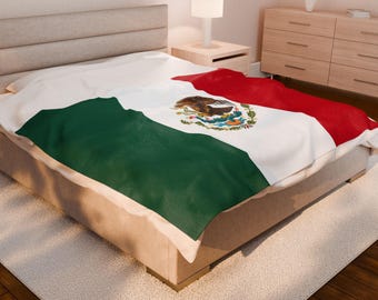 May include: A blanket draped over a bed, featuring the flag of Mexico. The design includes a green field, a white stripe with the Mexican coat of arms, and a red stripe. The blanket is made of a soft material and is displayed on a beige bed.