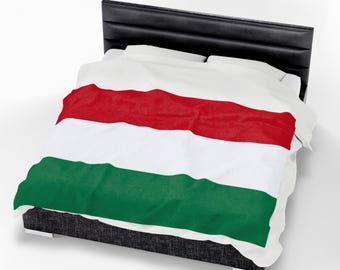 May include: A white blanket with a red, white, and green horizontal stripe design, draped over a bed. The bed has a black headboard and a dark gray base. The blanket's design resembles a flag.