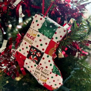May include: A red and green patchwork stocking ornament with the text "It's more than you ET" hanging on a Christmas tree.