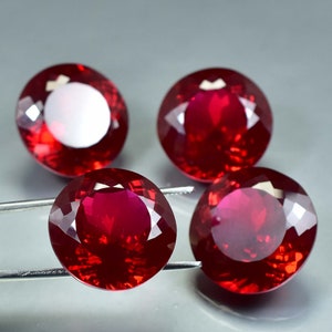 Peut inclure: Quatre pierres précieuses rondes, facettées, de couleur rouge. Les pierres précieuses sont serties dans un matériau transparent et réfléchissant.