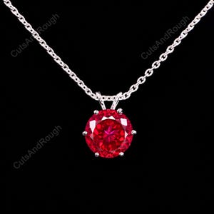 May include: A round, faceted, vibrant red gemstone pendant set in a silver-toned metal prong setting, suspended from a matching silver-toned chain. The text CutsAndRough is visible in the background, repeated in a diagonal pattern.