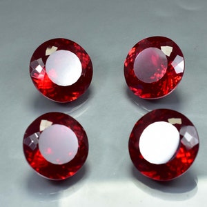 Pode incluir: Quatro pedras preciosas redondas de cor vermelha com corte facetado. As pedras preciosas est&atilde;o dispostas em forma de quadrado sobre uma superf&iacute;cie cinza.