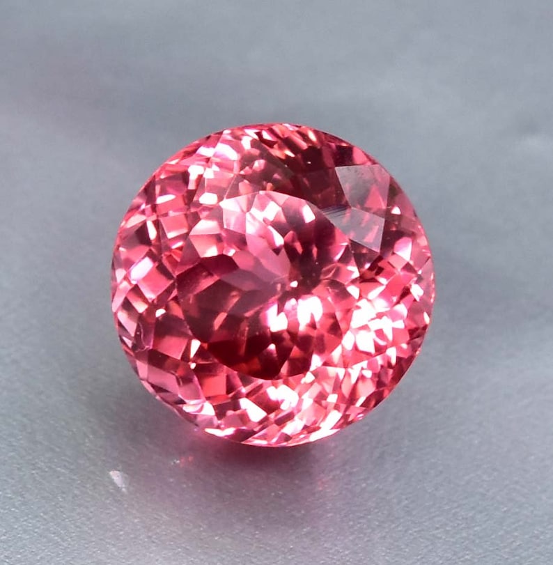 K&ouml;nnte beinhalten: Ein runder, facettierter rosa Edelstein mit hohem Glanz.