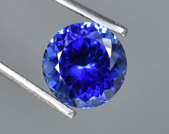 May include: A round, deep blue gemstone with a faceted cut. The gemstone is held in a pair of tweezers.