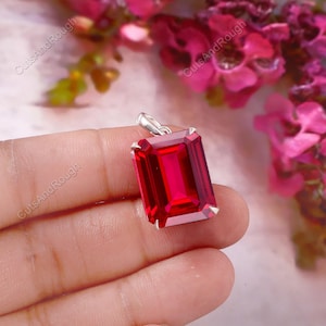 May include: A rectangular, faceted, vibrant red gemstone pendant set in a silver-toned metal prong setting. The pendant features a clear, deep red stone with sharp, clean edges and a polished finish, suspended from a small, integrated silver-toned bail.