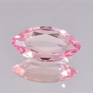 May include: A pink marquise cut gemstone with facets. The gemstone is on a reflective surface.