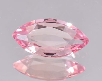 Puede incluir: Una piedra preciosa rosa de talla marquesa con facetas. La piedra preciosa está sobre una superficie reflectante.
