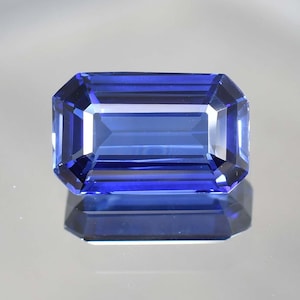 May include: A deep blue gemstone with an emerald cut. The gemstone is faceted and has a high polish.