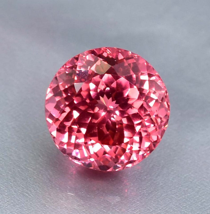 K&ouml;nnte beinhalten: Ein runder, facettierter rosa Edelstein mit einem brillanten Glanz.