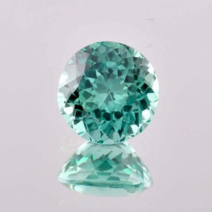 May include: A round, faceted gemstone with a light blue-green color. The gemstone is reflecting light, creating a sparkle effect.