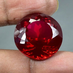 Puede incluir: Una piedra preciosa de color rojo intenso con forma redonda y superficie facetada.
