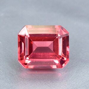 May include: A vibrant pink gemstone with a square emerald cut. The gemstone is faceted and has a high polish.