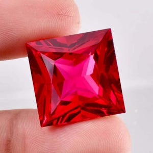 Puede incluir: Una gema roja vibrante de forma cuadrada con un patrón en forma de estrella en el centro.