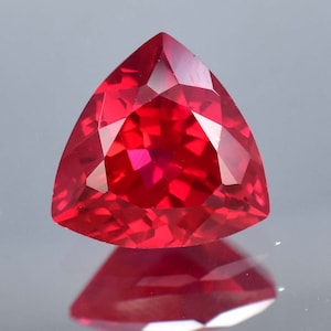 Peut inclure: Une pierre précieuse triangulaire rouge foncé avec une taille facetée. La pierre précieuse réfléchit la lumière et a une finition brillante.
