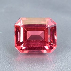 May include: A vibrant pink gemstone with a rectangular emerald cut.