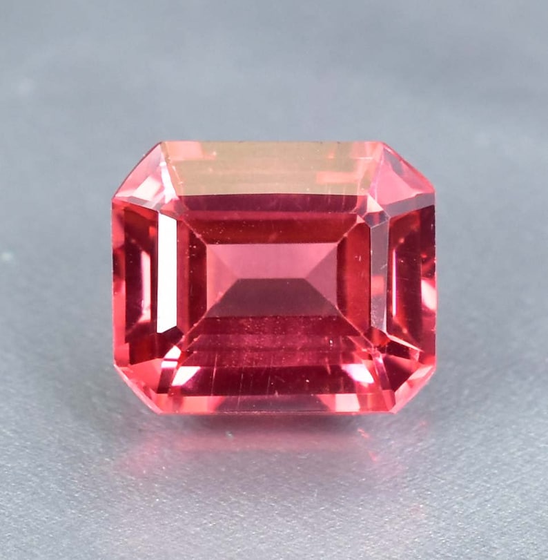 May include: A vibrant pink gemstone with a rectangular emerald cut.