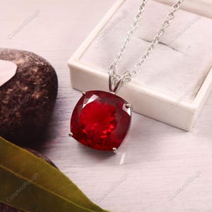 Op de afbeelding: Een zilveren ketting met een grote, vierkant geslepen, dieprode edelsteen hanger. De hanger is gezet in een zilveren bezel en hangt aan een fijne zilveren ketting. De edelsteen heeft een facetgeslepen oppervlak.