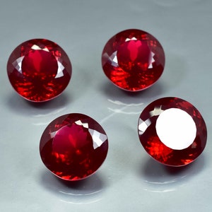 Pode incluir: Quatro pedras preciosas redondas de cor vermelha com alto polimento. As pedras preciosas est&atilde;o dispostas em um padr&atilde;o quadrado em uma superf&iacute;cie cinza.