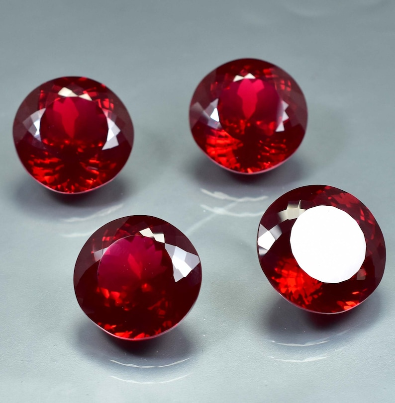 Pode incluir: Quatro pedras preciosas redondas de cor vermelha com alto polimento. As pedras preciosas est&atilde;o dispostas em um padr&atilde;o quadrado em uma superf&iacute;cie cinza.