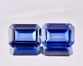 May include: Two blue emerald cut gemstones on a white background.