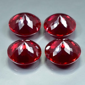 Pode incluir: Quatro pedras preciosas redondas, facetadas, de cor vermelha. As pedras preciosas s&atilde;o cortadas em forma redonda com uma parte superior pontiaguda.