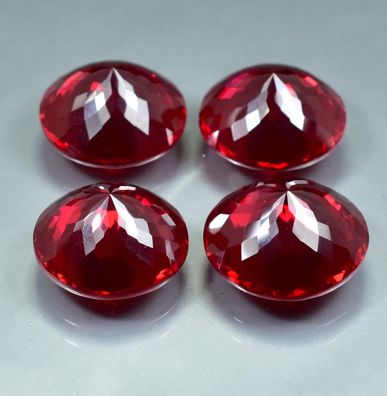 Pode incluir: Quatro pedras preciosas redondas, facetadas, de cor vermelha. As pedras preciosas s&atilde;o cortadas em forma redonda com uma parte superior pontiaguda.