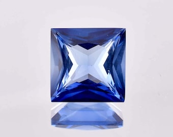 May include: A square-shaped, blue gemstone with a faceted cut. The gemstone is reflecting light, creating a bright, blue shine.
