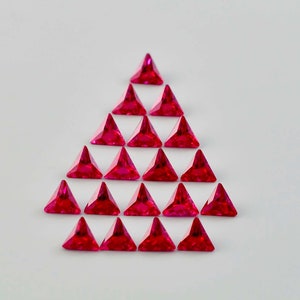 May include: A triangular arrangement of twenty-one red triangular gemstones. The gemstones are arranged in a pyramid shape, with the largest gemstone at the top and the smallest gemstones at the bottom.