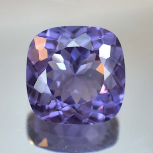 May include: A cushion-cut amethyst gemstone with a purple hue and a faceted design.