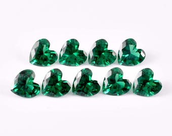 May include: Ten heart-shaped, faceted gemstones in a vibrant emerald green hue are arranged on a white surface. The gemstones are cut to maximize light reflection, creating a sparkling effect. These gems could be used for jewelry making or other crafts.