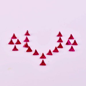 Puede incluir: Una colección de 18 piedras preciosas triangulares de color rojo rubí dispuestas en forma de corazón sobre un fondo blanco.