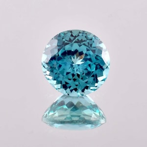 May include: A round, faceted gemstone with a blue-green hue. The gemstone is reflecting light, creating a star-like pattern in the center.