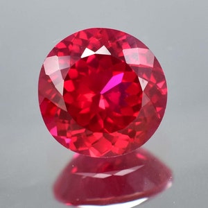 Op de afbeelding: Een levendige rode edelsteen met een ronde vorm en een gefacetteerd oppervlak. De edelsteen reflecteert licht, waardoor een sprankelend effect ontstaat.