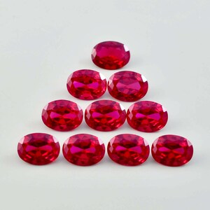 May include: Ten oval-shaped, deep red gemstones arranged in a pyramid shape on a white background.